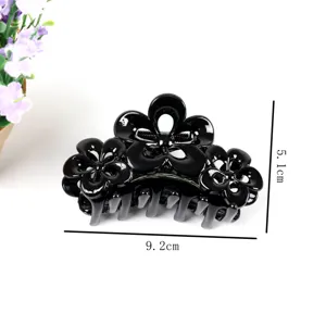 Close-up detail view of the black flower hair claw clip, showing its glossy finish and size.