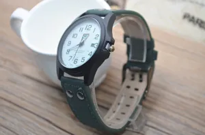 Men's military quartz watch with black matte case and green leather strap detail view.