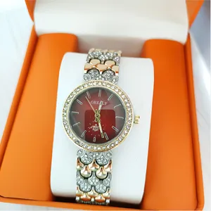 Gros-plan de montre quartz femme luxe, cadran rouge dégradé, lunette strass et bracelet bicolore.