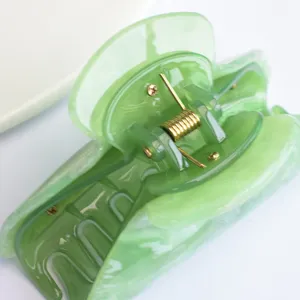 Primo piano di una molletta per capelli in acrilico verde con motivo nebbia d'acqua e molla.