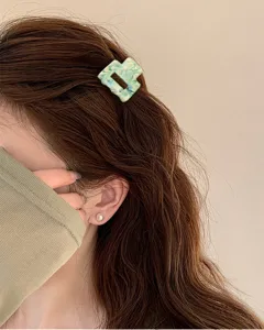 Dettaglio in primo piano della molletta per capelli geometrica marmorizzata verde.