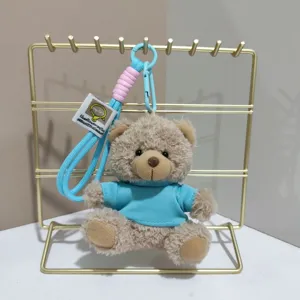 Plush teddy bear keychain detail view, cute blue outfit, soft toy hanging on rack.
