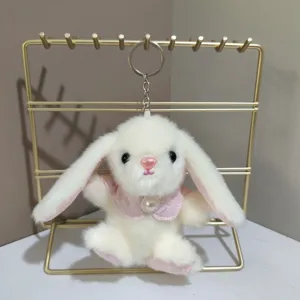 Schattige witte pluche konijn sleutelhanger met roze cape op een gouden displaystandaard.