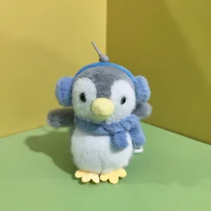 Dettaglio del simpatico peluche di pinguino, con paraorecchie e sciarpa blu, morbido ciondolo.
