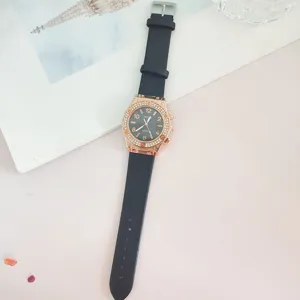 Montre à quartz tendance avec bracelet en cuir noir, lunette strass or rose et chiffres.