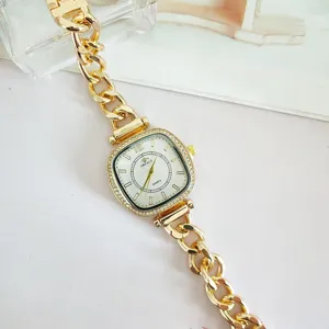 Primer plano del lujoso reloj de mujer cuadrado con pedrería y pulsera de cadena dorada.