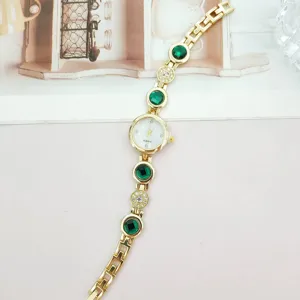 Nahaufnahme Detail der goldenen Damen Quarz Armbanduhr mit grünen Steinen und Strasssteinen.