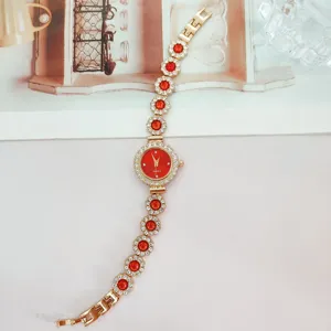 Detailaufnahme der goldenen Damen Quarzurhr mit roten runden Steinen und funkelnden Kristallen.