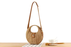 Handmade woven straw crossbody bag detail, featuring round ring handle and brown leather strap.