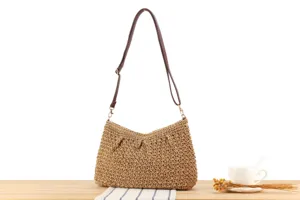 Vue détaillée d'un sac à bandoulière en paille tressée fait main avec lanière en cuir sur table.
