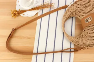 Detail view of handmade woven straw crescent crossbody bag with leather strap and lock.