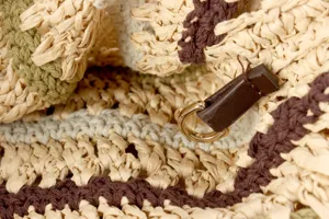 Handcrafted woven shoulder bag detail showing fine texture, metal ring and contrast stripes.