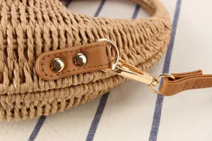 Close-up detail of straw woven handbag with gold hardware and brown leather strap.