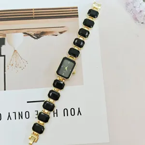 Close-up of women's quartz watch with a rectangular black dial and gold gemstone link bracelet.