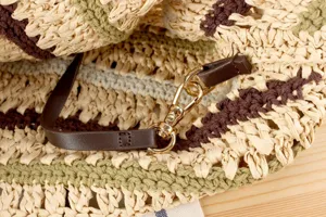 Handmade crochet straw shoulder bag detail with leather strap and gold metal lobster clasp.