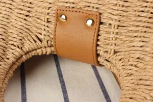 Close-up detail of hand-woven straw bag texture, brown pu leather tab and gold rivets.