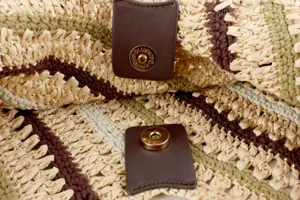 Close-up detail of the magnetic snap closure and woven straw texture on the fashion bag.