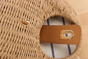 Close-up of handmade woven straw bag detail with leather strap and golden lock fastener.