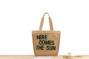 Detail view of large woven straw tote bag featuring chic green embroidered text and dual handles.