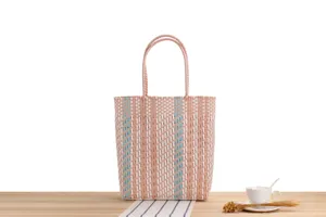 Dettaglio borsa intrecciata rosa e bianca con struttura in plastica su tavolo in legno.