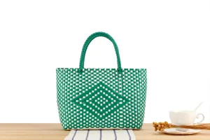 Primo piano dettaglio di borsa intrecciata verde e bianca su tavolo in legno con tazza.