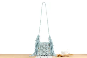Detail view of handmade light blue macrame woven shoulder bag with delicate fringe and knots.