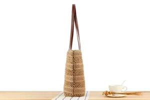 Detailed side view of a stylish straw woven tote bag with brown leather straps for women.
