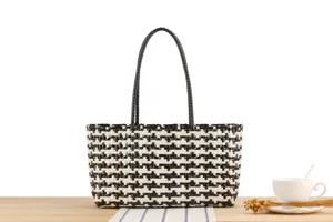 Black and white woven plastic tote bag detail, casual beach handbag on wooden table.