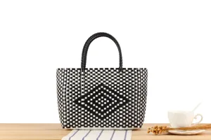 Dettaglio ravvicinato della borsa in plastica intrecciata nera e bianca con motivo a losanga.