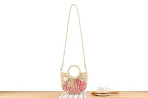 Close-up detail of handmade woven straw crossbody bag with pink doll letters and round handle.
