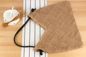 Vista detallada del bolso de hombro triangular de paja tejida a mano con correa negra elegante.