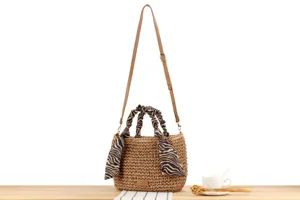 Woven straw shoulder bag with zebra print scarf handle and adjustable leather strap detail.