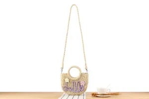 Detailed view of handmade woven straw crossbody bag with cute flower and hello embroidery.