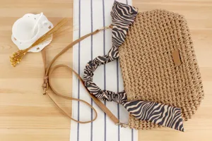 Detailed view of handmade woven straw crossbody bag featuring trendy zebra print scarf wrapped handle.