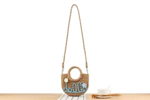 Detailed view of a handmade woven straw crossbody bag with floral and letter decor