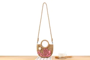 Detailed view of handmade woven straw crossbody bag featuring cute pink Hello text decor.