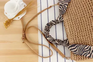 Handwoven straw shoulder bag with chic zebra print scarf handle and detachable brown strap.