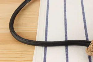 Primer plano del asa de cuero negro y textura de paja tejida para bolso de paja elegante.