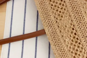 Close-up of straw woven shoulder bag detail, featuring natural mesh texture and brown leather strap.