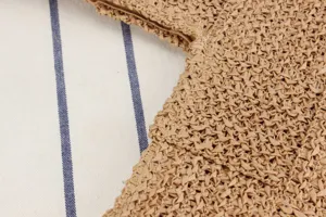 Vista de detalle del bolso de hombro de paja marrón, mostrando una fina textura artesanal.