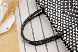 Primo piano dettagliato del manico e del motivo a quadri di una borsa in plastica intrecciata.