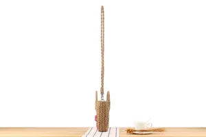 Detailed view of handmade straw woven crossbody and handbag with pink flower accent.