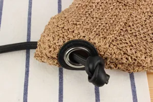 Primer plano del detalle del bolso de paja tejido a mano con cordón de cuero y ojal metálico.