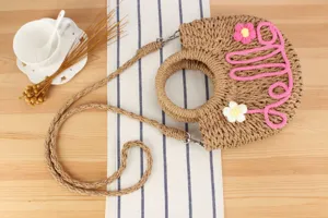 Handmade straw woven crossbody bag detail, featuring cute flower decor and letter design.