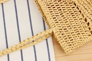 Close-up detail of a handmade straw woven shoulder bag, showing fine texture and braided handles.