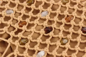 Detail shot of beige woven mesh handbag fabric featuring elegant colorful stone beads.