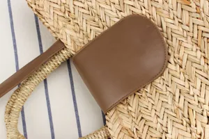 Primo piano sui dettagli della borsa in paglia intrecciata con patta in pelle PU marrone.
