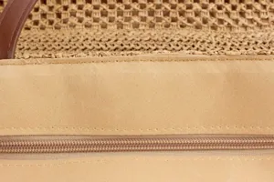 Close-up detail of the woven straw handbag featuring a brown leather handle and secure zipper.