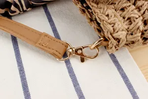 Detail view of women straw woven bag strap with gold metal hardware and brown leather trim.