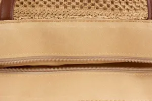Detailed close-up of straw woven tote bag interior, showing zipper, lining and brown strap.